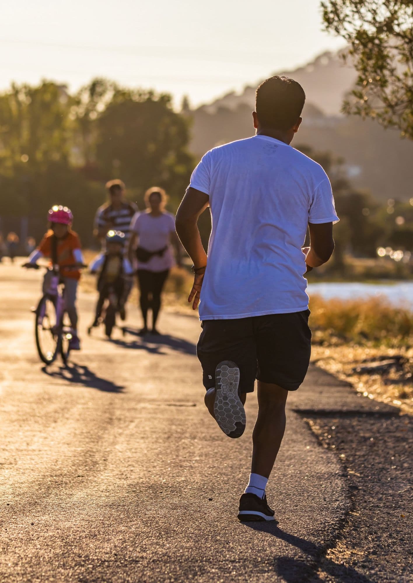A man in a white T-shirt runs along a path at golden hour, seen from behind.