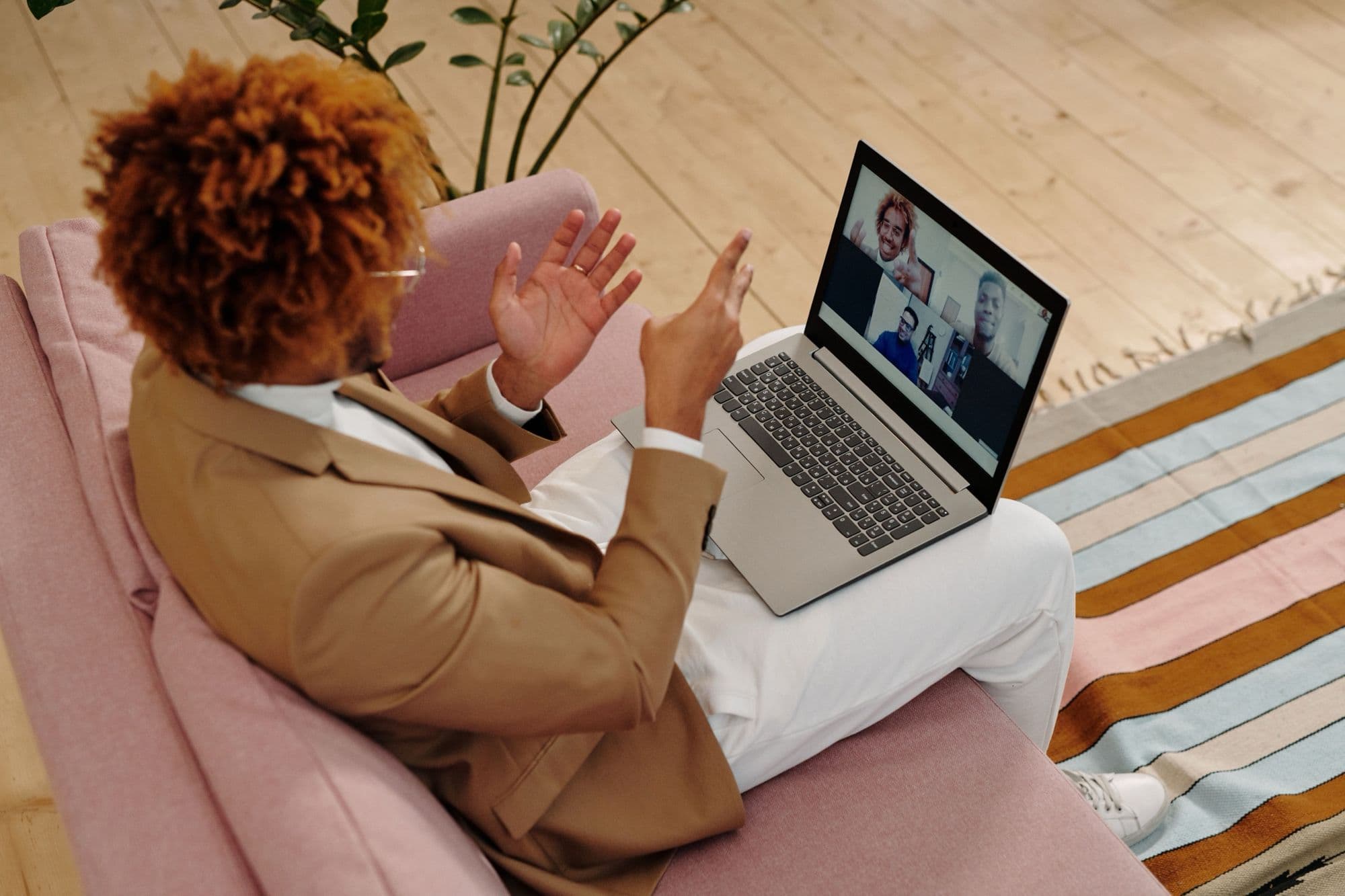 A man in a camel blazer on a sofa talks with his hands during a video call on his laptop.
